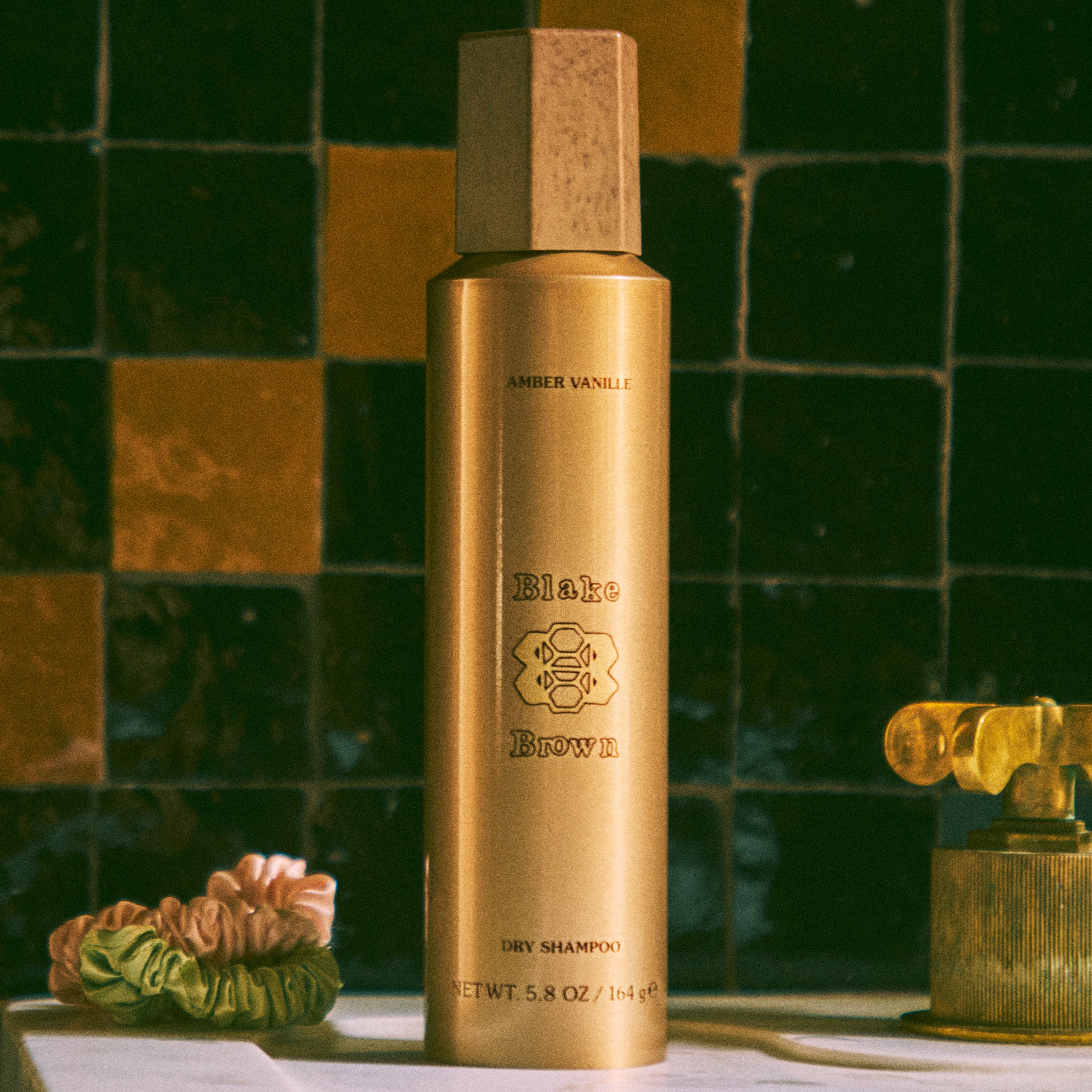 Blake Brown Dry Shampoo by Blake Lively in a luxurious bathroom scene next to hair scrunchies, conveying its mainstay as a haircare essential.